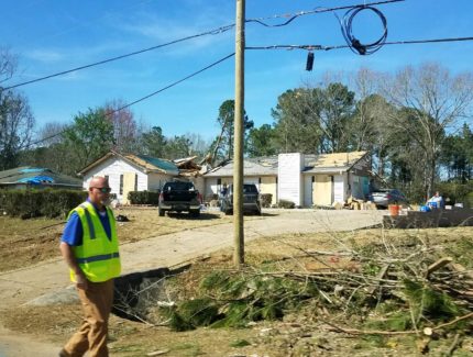 A man walks past a house surrounded by fallen trees.