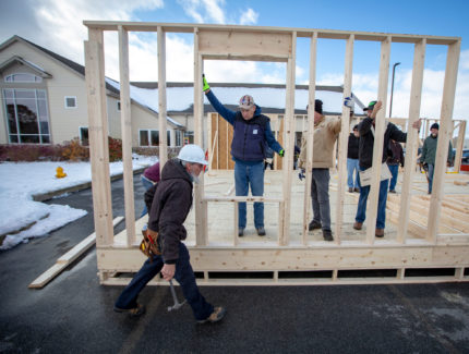 Several men hold up a framed wall while building a house.