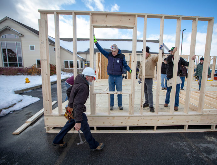 Several men hold up a framed wall while building a house.