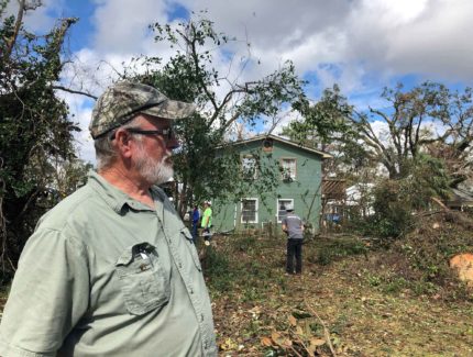 A man looks at fallen trees in his yard.