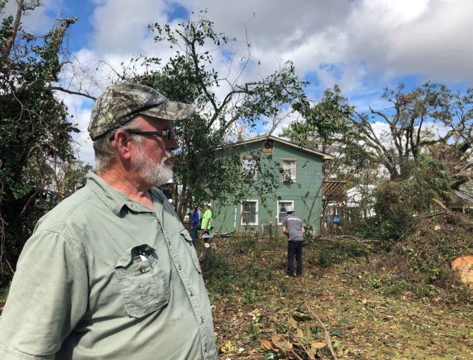 A man looks at fallen trees in his yard.