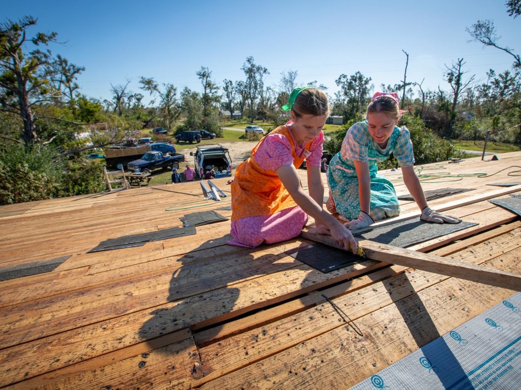 Two volunteers cutting shingles for roof on the roof