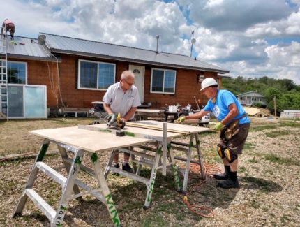 Two men working on a table in front of a house.