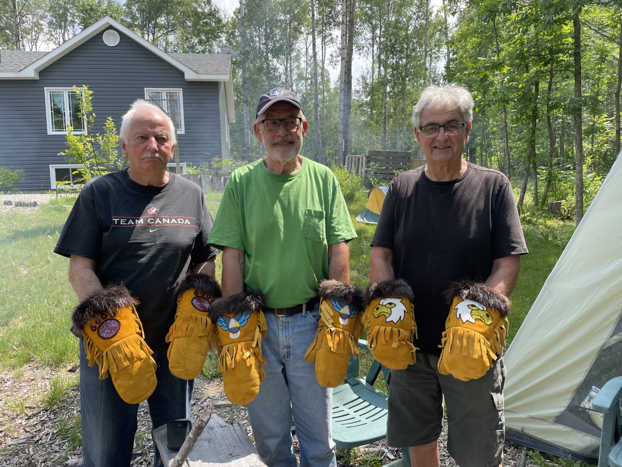 Three men holding mitts in the woods.