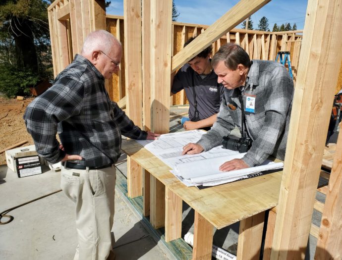 A group photo of volunteers looking at blue prints on a job site in Paradise, California.