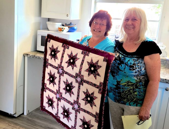 Two women photographed with quilted wall hanging to celebrate the completion of an MDS project in Marianna, FL