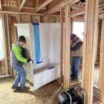 Two volunteers moving a tub and shower combo through a framed interior space.