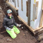 One of the three amigos working on a foundation while kneeling in dirt.