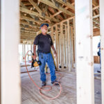 Longterm volunteer standing with a nail gun surrounded by freshly framed walls of a new build in Welsh, LA
