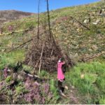 a volunteer in a bright pink dress throws lumber onto a burn pile in the middle of lush greenery