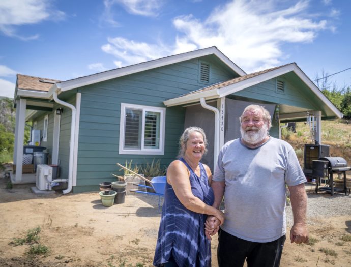 Homeowners stand in front of their new home, brightly painted green to offset the loss of vegetation after the Camp fire.