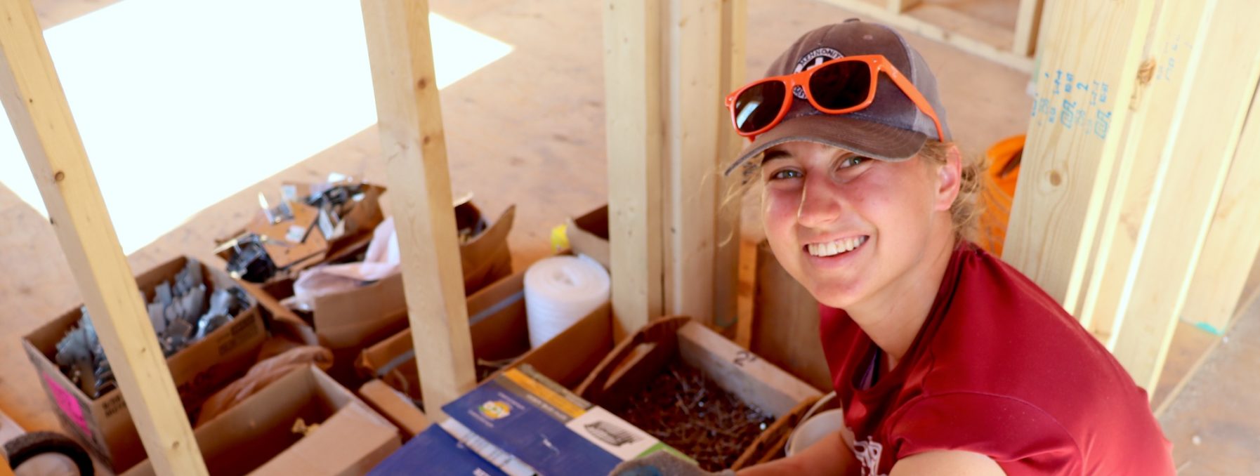 Sofia Epp, an MDS volunteer, sifts through tools at a new build and glances up at the camera for a picture