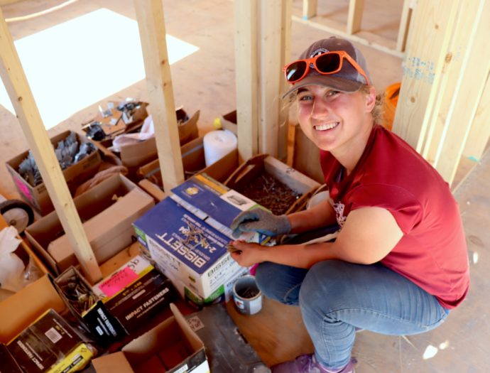 Sofia Epp, an MDS volunteer, sifts through tools at a new build and glances up at the camera for a picture