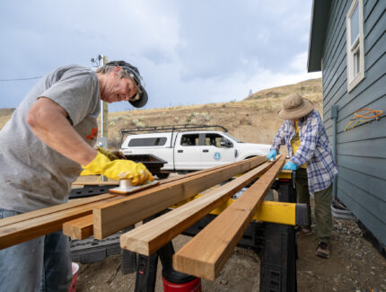A couple volunteers work on long wood planks outside a new build