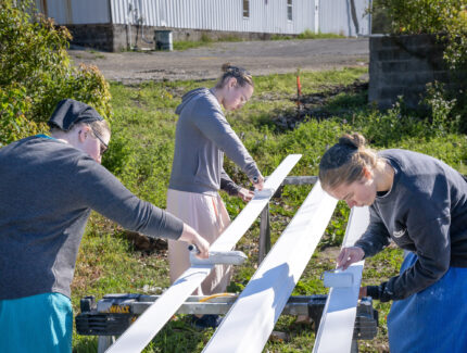 Three volunteers work on painting trim outside during spring time.