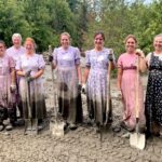 7 Traditional women stand in muddy dresses holding shovels after a long day mucking out mud.