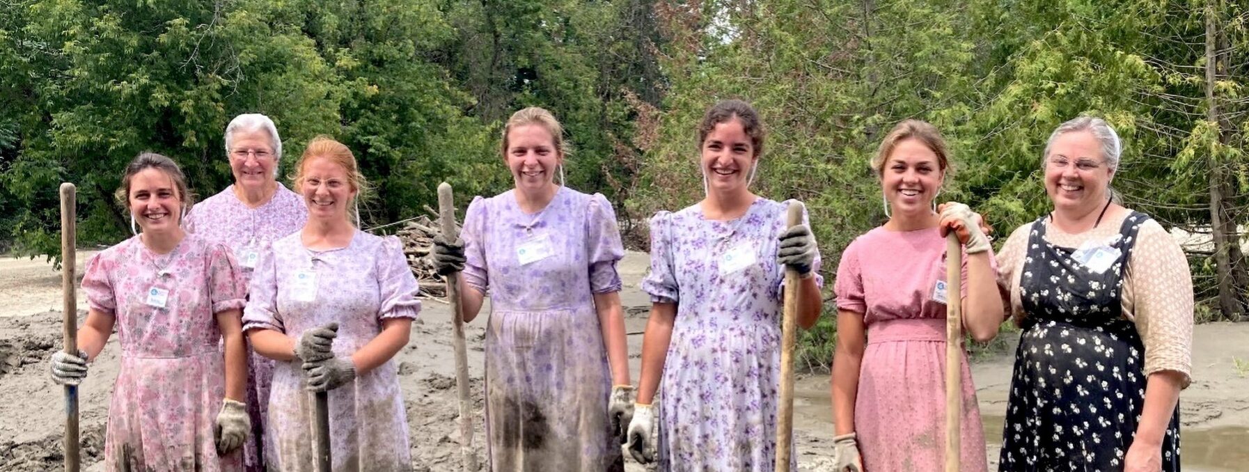 7 Traditional women stand in muddy dresses holding shovels after a long day mucking out mud.