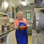 A woman wearing oven mitts holds a pot in a mobile kitchen
