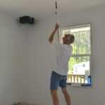 A man rolls paint onto a ceiling
