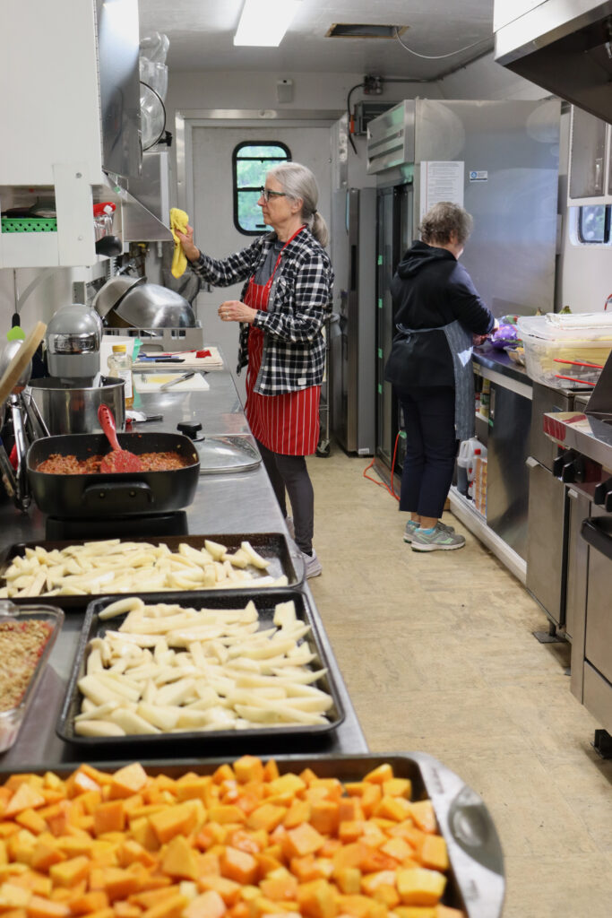 Two cooks prepare a volunteer dinner in a kitchen trailer.