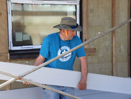 A volunteer prepares to install siding on a house