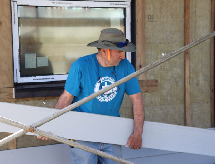 A volunteer prepares to install siding on a house