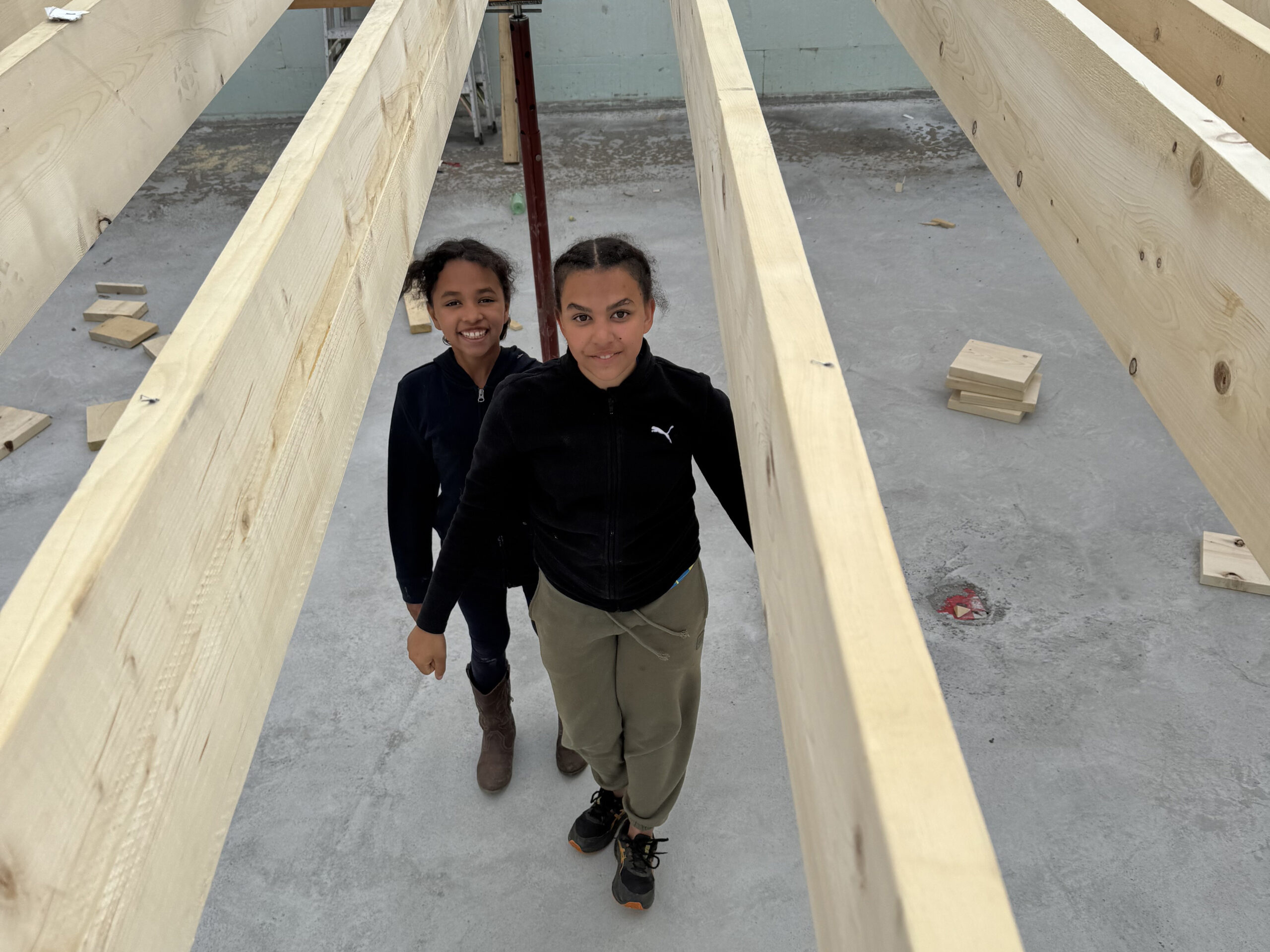 Two girls stand in the crawlspace of a house under construction