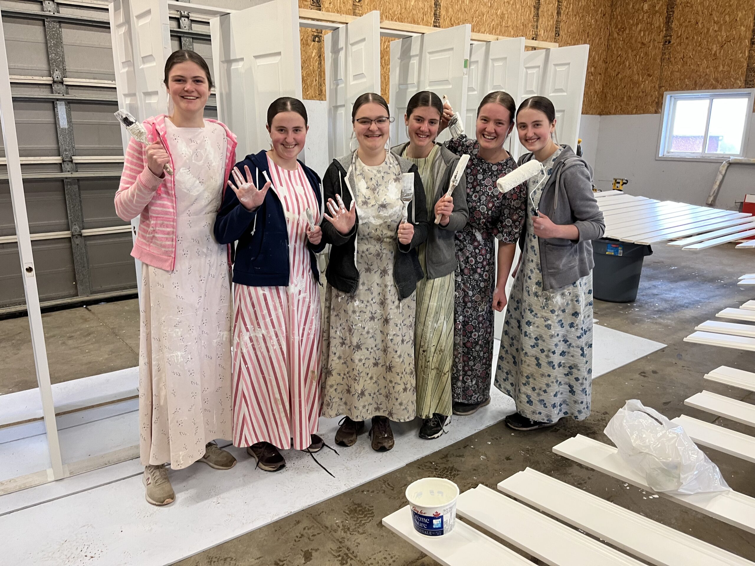 Young women hold up paint rollers in front of freshly painted doors