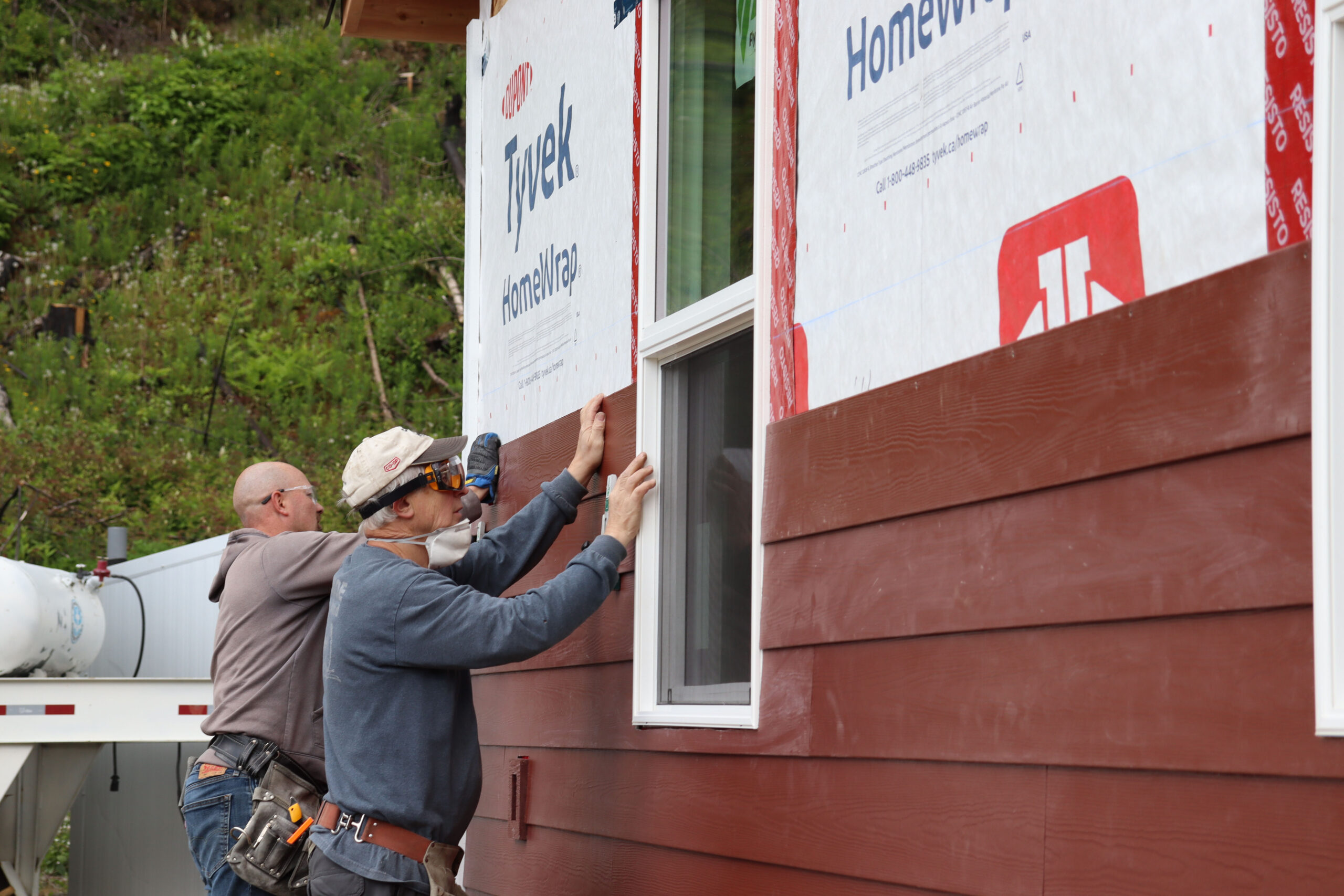 Two volunteers install siding on a house