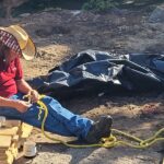 Man sits on lumber stack braiding rope.