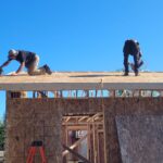 Two men install sheeting on roof for new house build.
