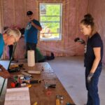 Three people stand around table, preparing tools for construction.