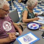 Two people sit at a table painting.