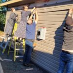 Four people attaching siding to a new house build.