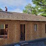 A house under constrution with three workers on top doing roofing.