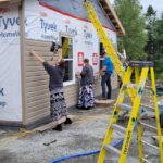 Three volunteers work to instal siding to a house.
