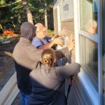 Three volunteers work at fitting siding to a new house build.