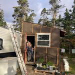 Woman standing in a doorway, holding open the door of her home underconstruction.