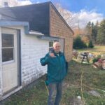 Man stands in front of his house, smiling.