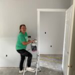 Woman with one foot on stepladder, holding a paint can and brush.