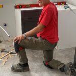 Man kneeling on one knee installing kitchen cabinets.