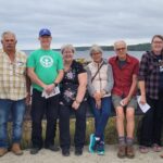 Group of people stand in front of body of water, posing for a group picture.