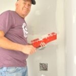 Man smiles while holding tools for plastering walls.