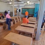 a group of people spread about a classroom with wooden desks.