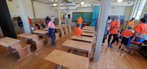 a group of people spread about a classroom with wooden desks.