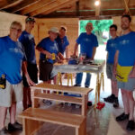 Group of people stand around a desk that they are constructing.