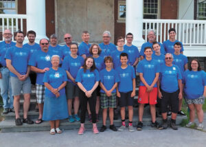 Group of people in blue shirts stand for picture outside old school building.