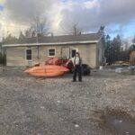 Man stands with his house in the background, as well as a tractor and canoe.