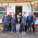 Group of people stand in front of house under construction.
