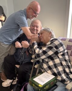 Man, standing, hugs couple who are sitting.